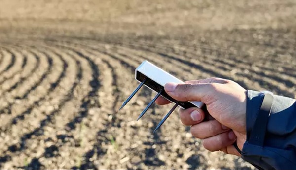 A hand holding a device with spikes in the background

Description automatically generated